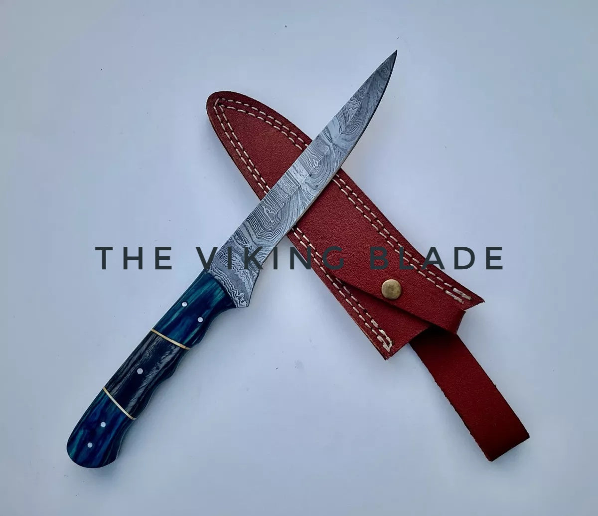 A custom handmade Damascus steel filet kitchen knife with a leather sheath. The knife has a blue and red handle with a patterned blade and a brass bolster.