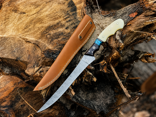 A fixed-blade knife with a silver steel blade, black and blue handle, and cream-colored handle scale, shown next to its brown leather sheath on a rustic log outdoors.