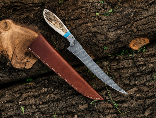 A fixed-blade knife with a patterned steel blade, a natural bone handle, and a brown leather sheath, arranged diagonally on a textured tree bark background.