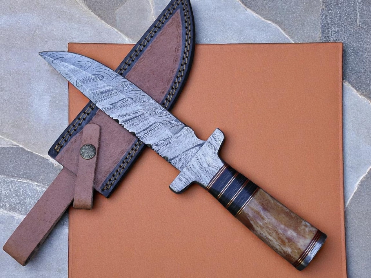A custom handmade Damascus steel hunting knife with a brown leather sheath, displayed on an orange surface. The knife has a silver blade with visible layering and a wooden handle.