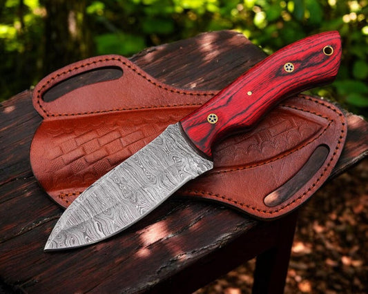 A Damascus steel hunting knife with a red leather sheath, featuring a clip point blade design.