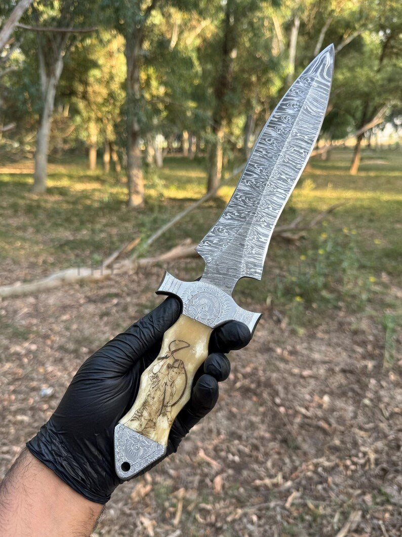 Hand holding a knife with a detailed blade and wooden handle outdoors.