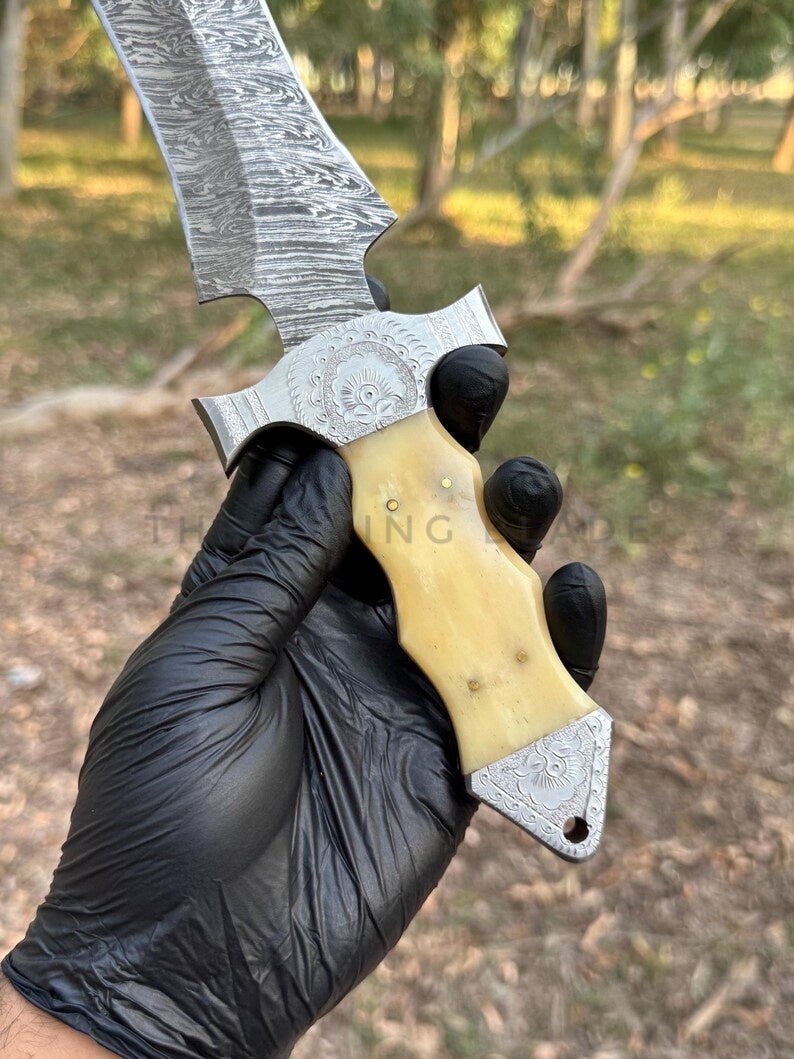 Hand holding a knife with a decorative blade and wooden handle, outdoors.