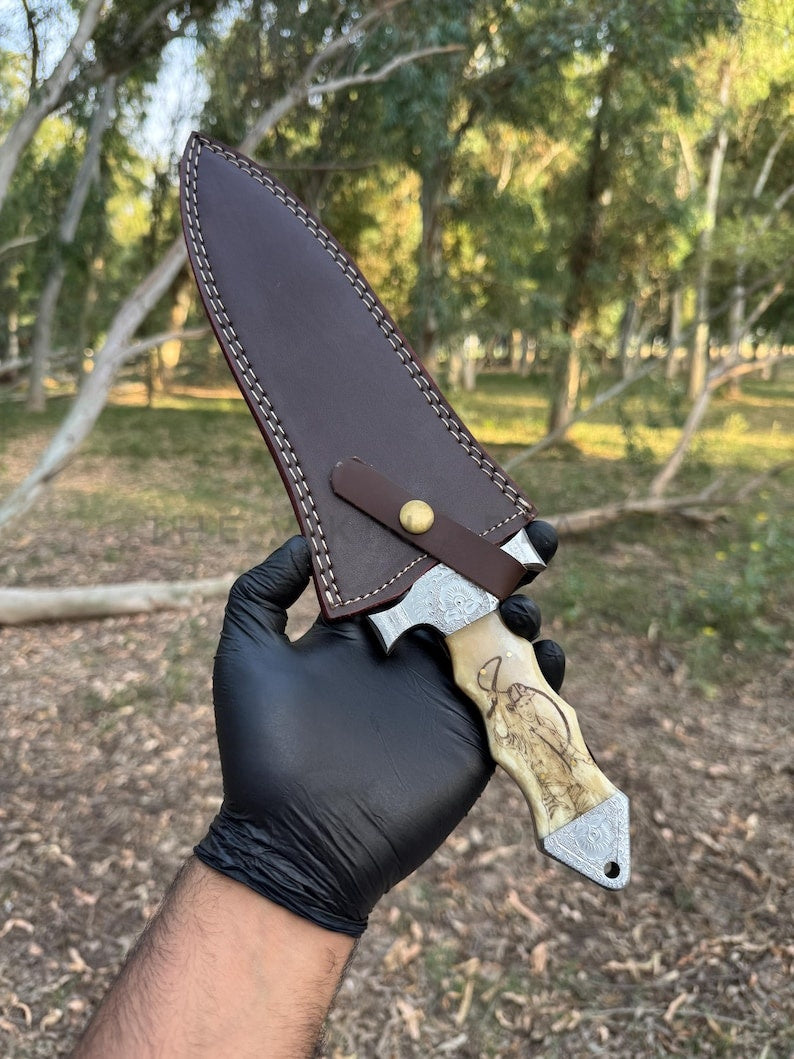 Knife with wooden handle and leather sheath held by a gloved hand in a forest setting