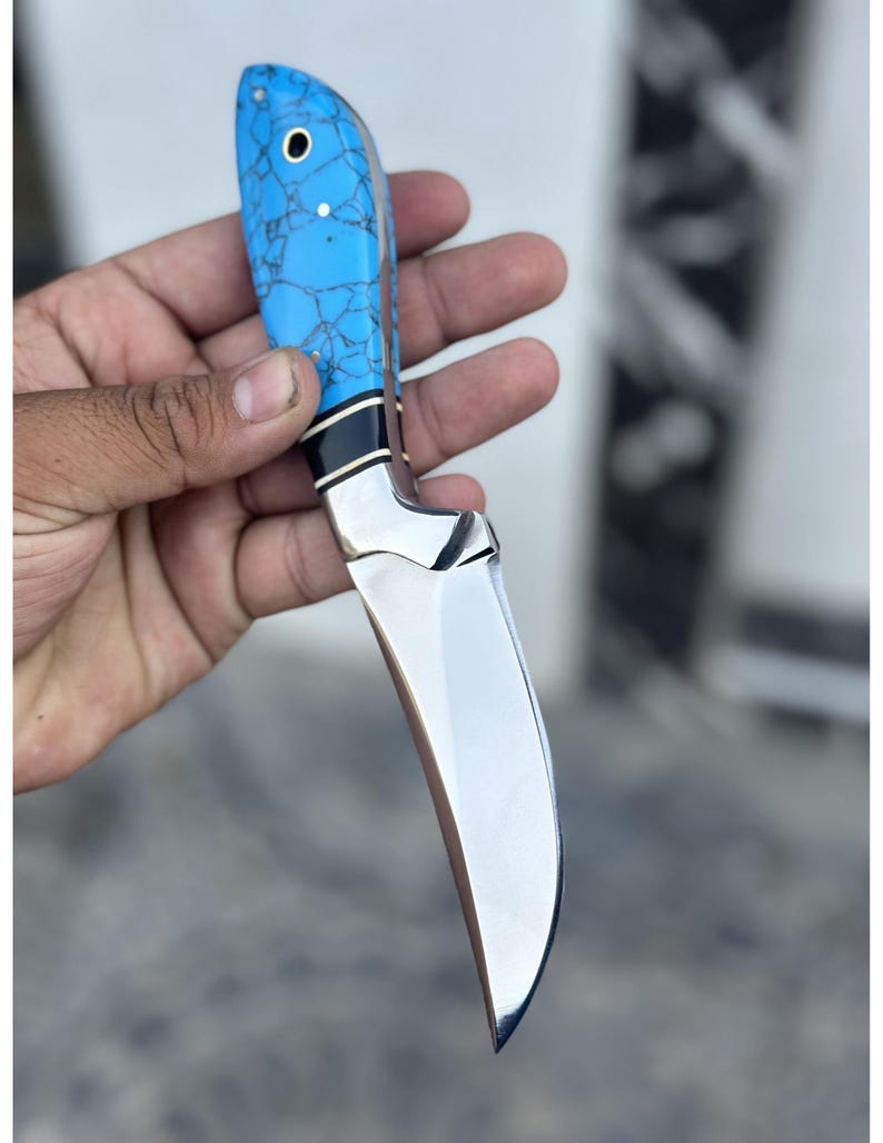 Hand holding a knife with a blue handle against a blurred background