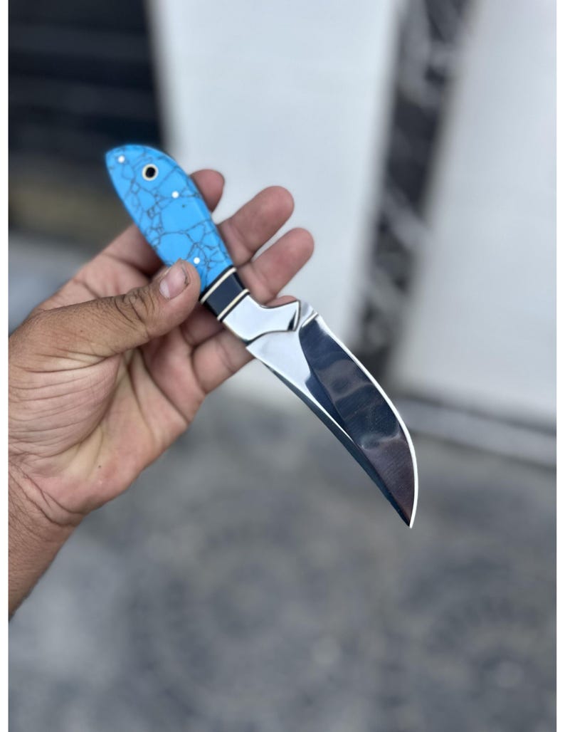 Hand holding a knife with a blue handle against a blurred background