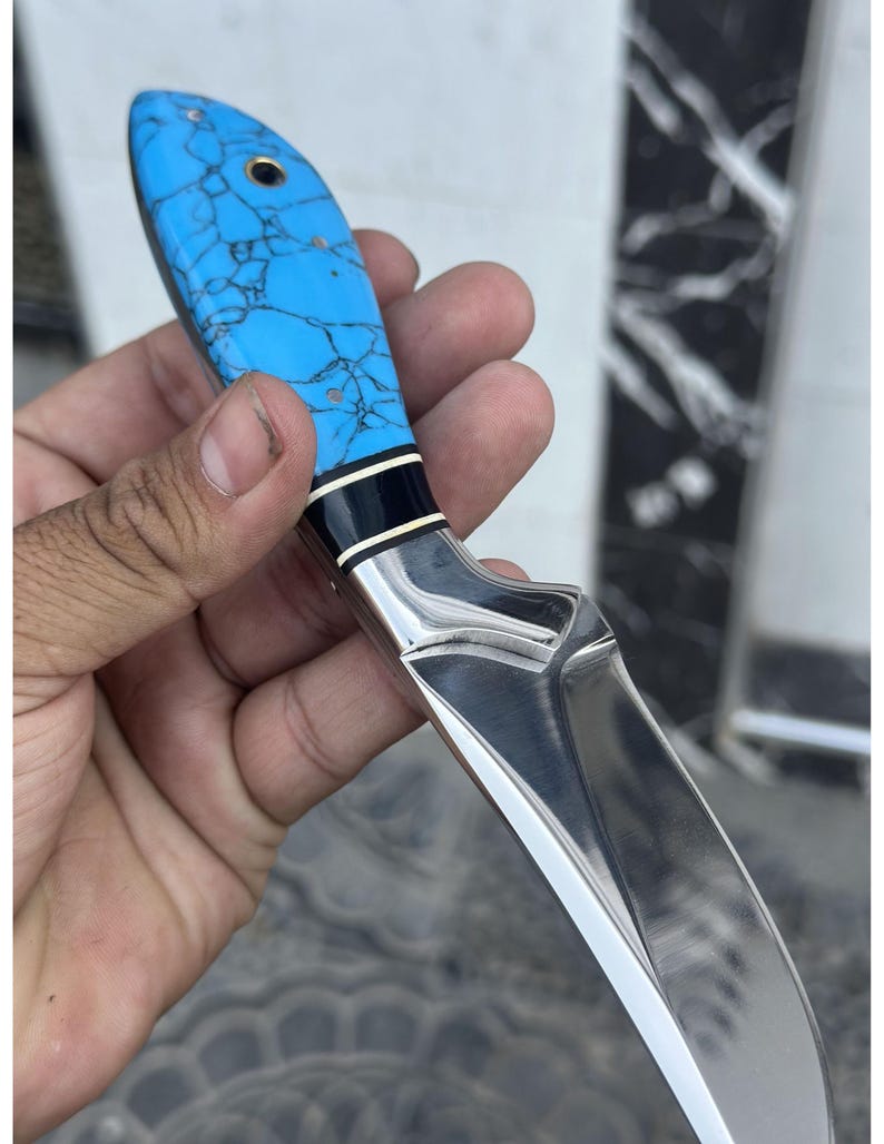 Hand holding a knife with a blue handle and silver blade against a blurred background