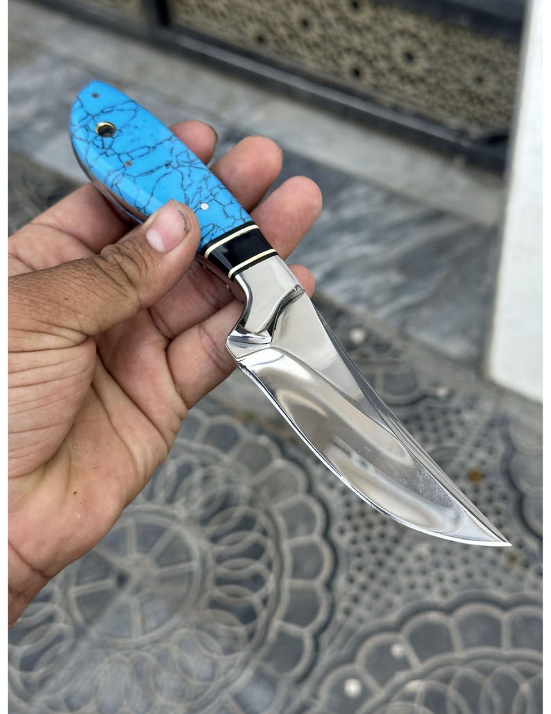 Hand holding a knife with a blue handle on a textured surface