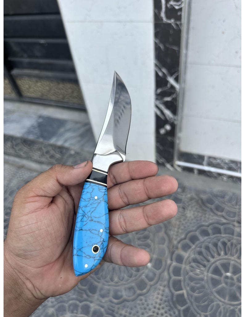 Hand holding a knife with a blue handle against a tiled floor background