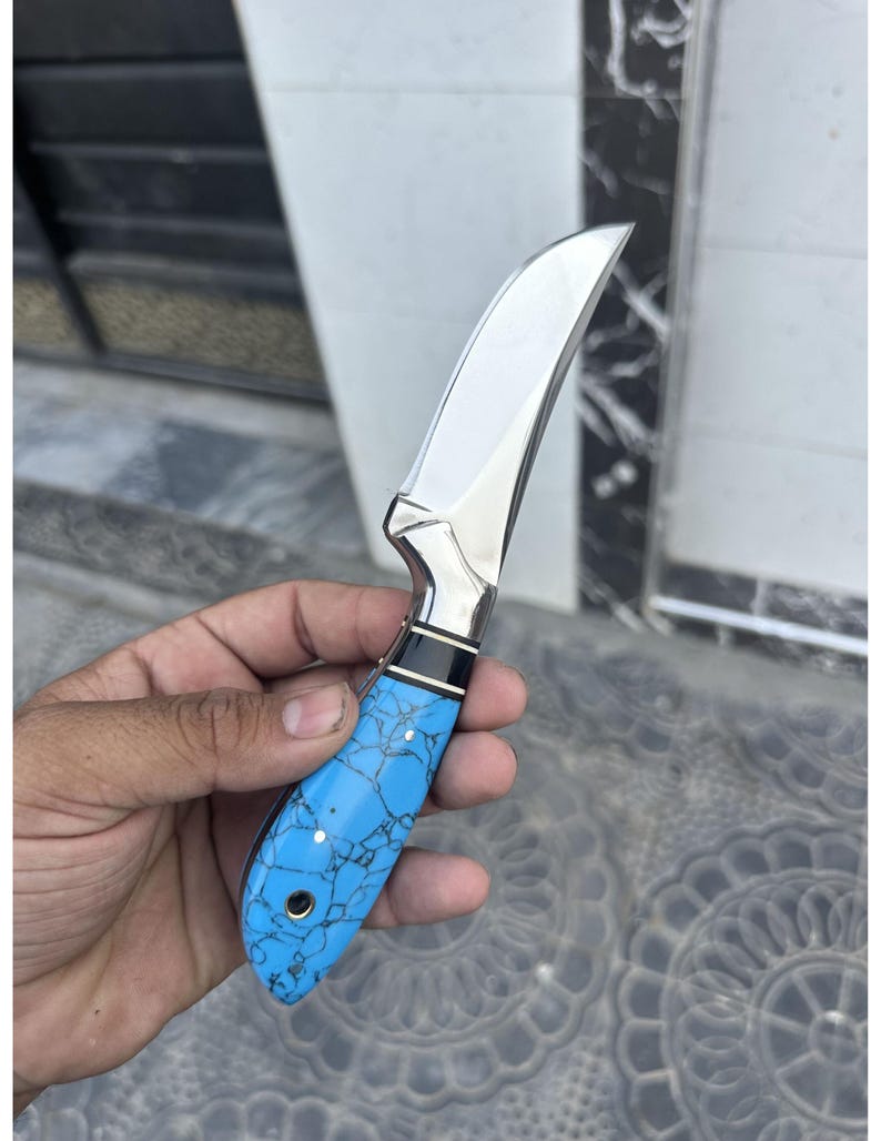 Knife with a blue handle held by a hand on a textured surface