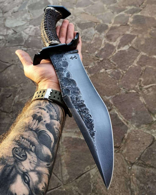 Hand holding a large knife with a textured blade and decorative handle on a stone surface.
