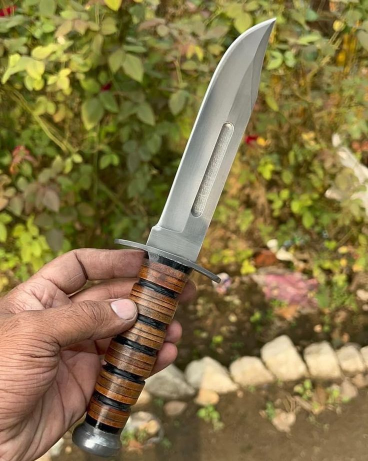 Hand holding a knife with a wooden handle against a natural background