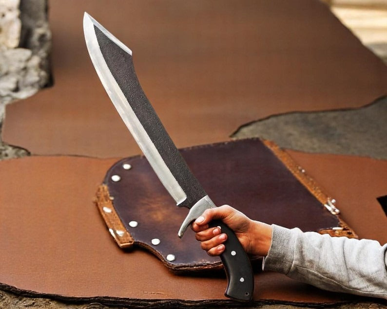 Handmade hunting knife with a twisted blade design, held in a person's hand, with a brown leather sheath in the background.