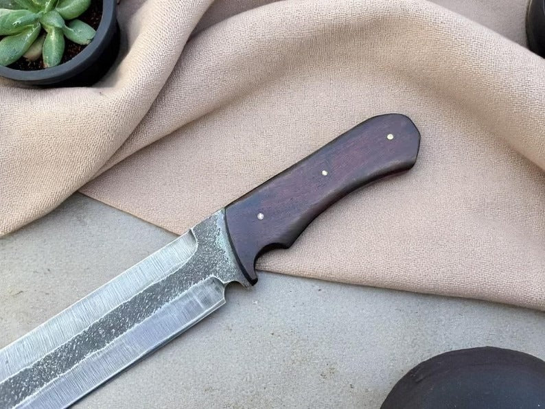 A handmade hunting seax knife with a wooden handle and a natural leather sheath, displayed on a beige fabric surface.