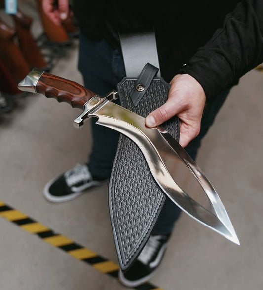 Person holding a kukri knife with a sheath on a blurred background