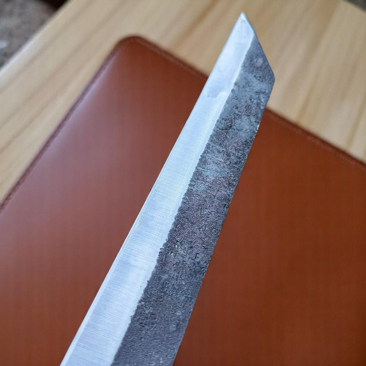 Close-up of a sword blade with a brown leather object in the background.