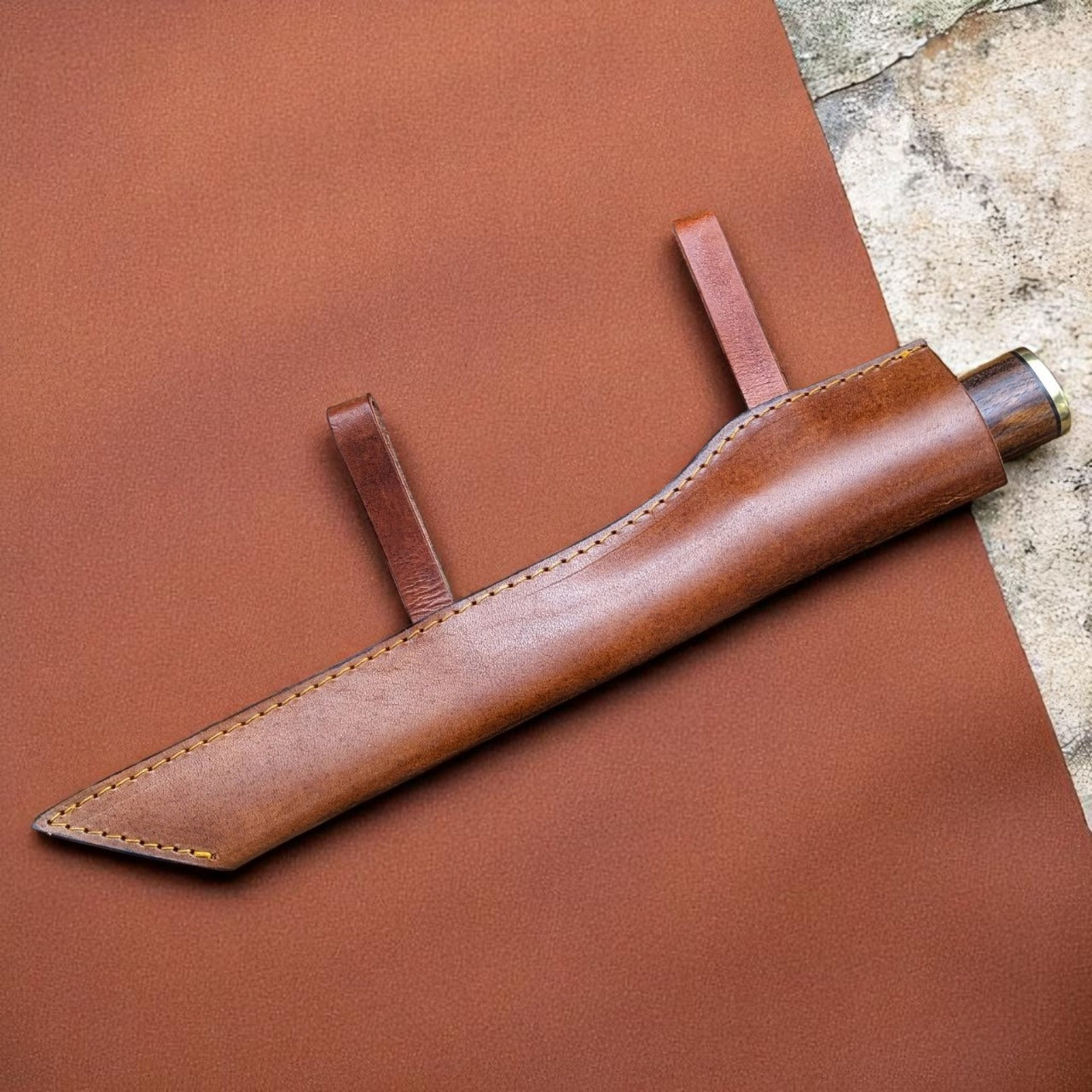 Brown leather knife sheath on a larger piece of brown leather.