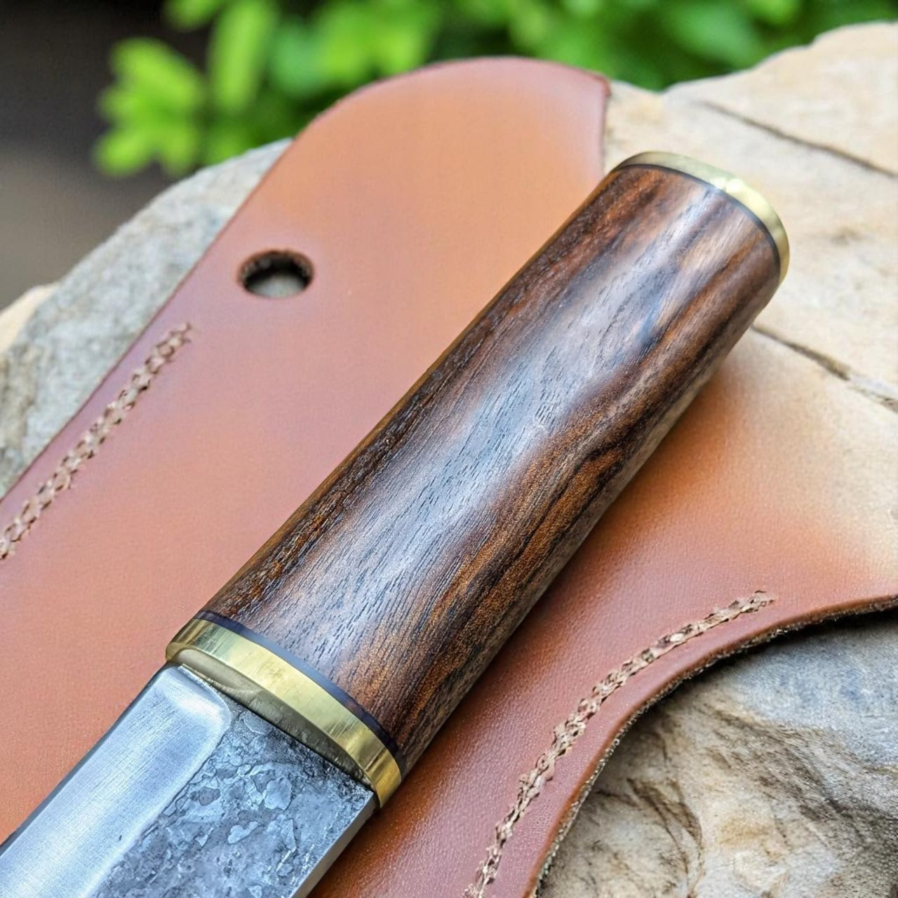 Knife with wooden handle and leather sheath on a rock.
