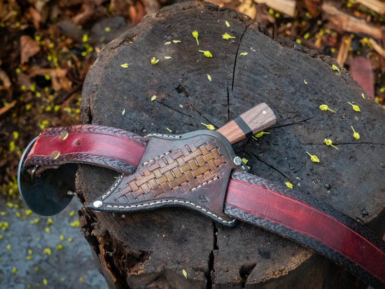 Handmade knife sheath with leather and wood details on a tree stump.