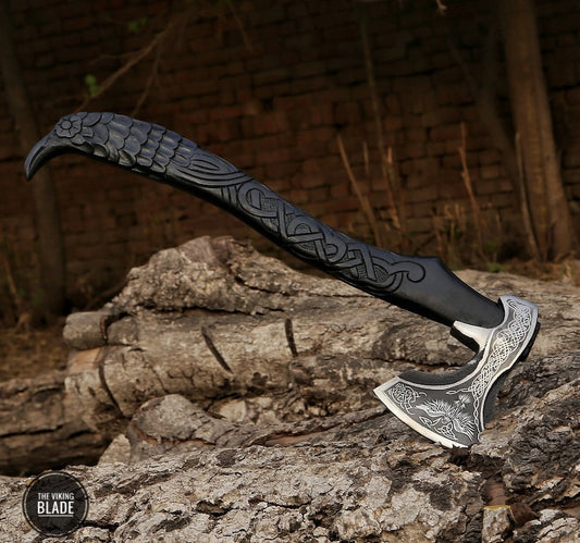 A hand-forged carbon steel Viking axe with a black leather-wrapped handle featuring Norse mythology-inspired engravings, resting on a wooden stump with a natural background.