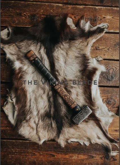 Decorative axe with ornate handle on a fur rug against a wooden background, featuring 'The Viking Blade' branding.