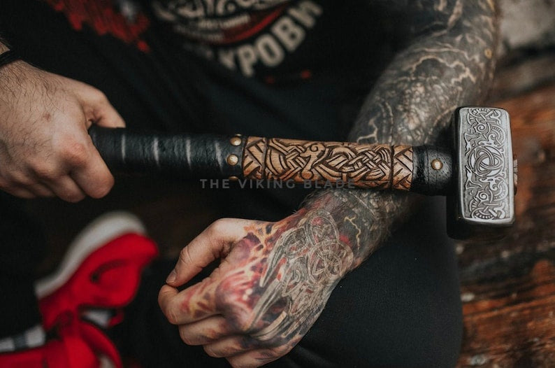 Person holding a decorated hammer with intricate designs, wearing a dark jacket with red accents.