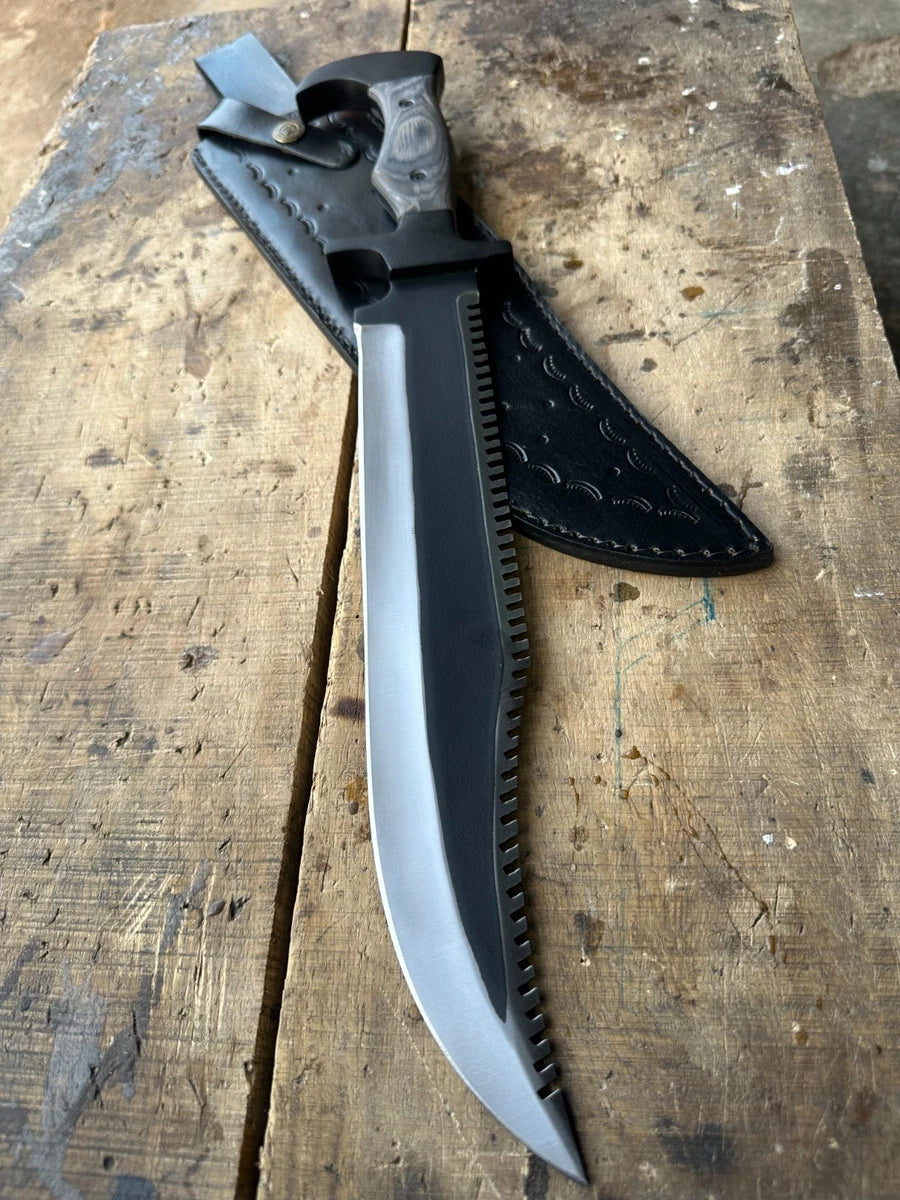 A large fixed-blade knife with a curved silver blade and black handle, shown partially sheathed on a worn wooden surface. The sheath is black leather with visible stitching.