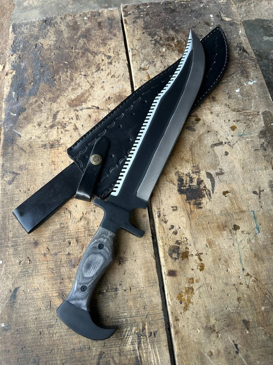 A large fixed-blade knife with a black serrated blade, black handle, and black leather sheath, displayed diagonally on a rustic, weathered wooden surface.