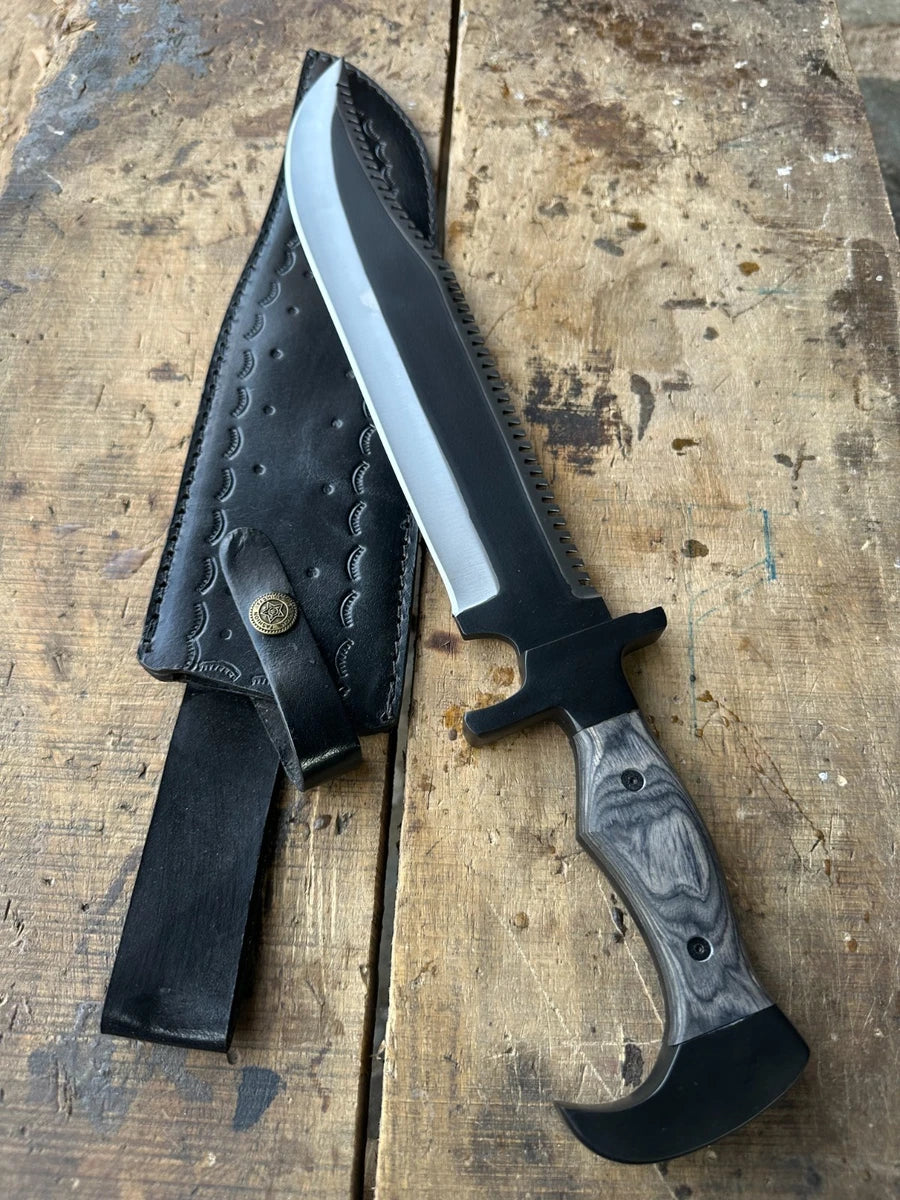 A fixed-blade knife with a satin-finished silver blade, black bolster and guard, and a gray marbled handle, shown next to its black stitched leather sheath on a rustic wooden surface.