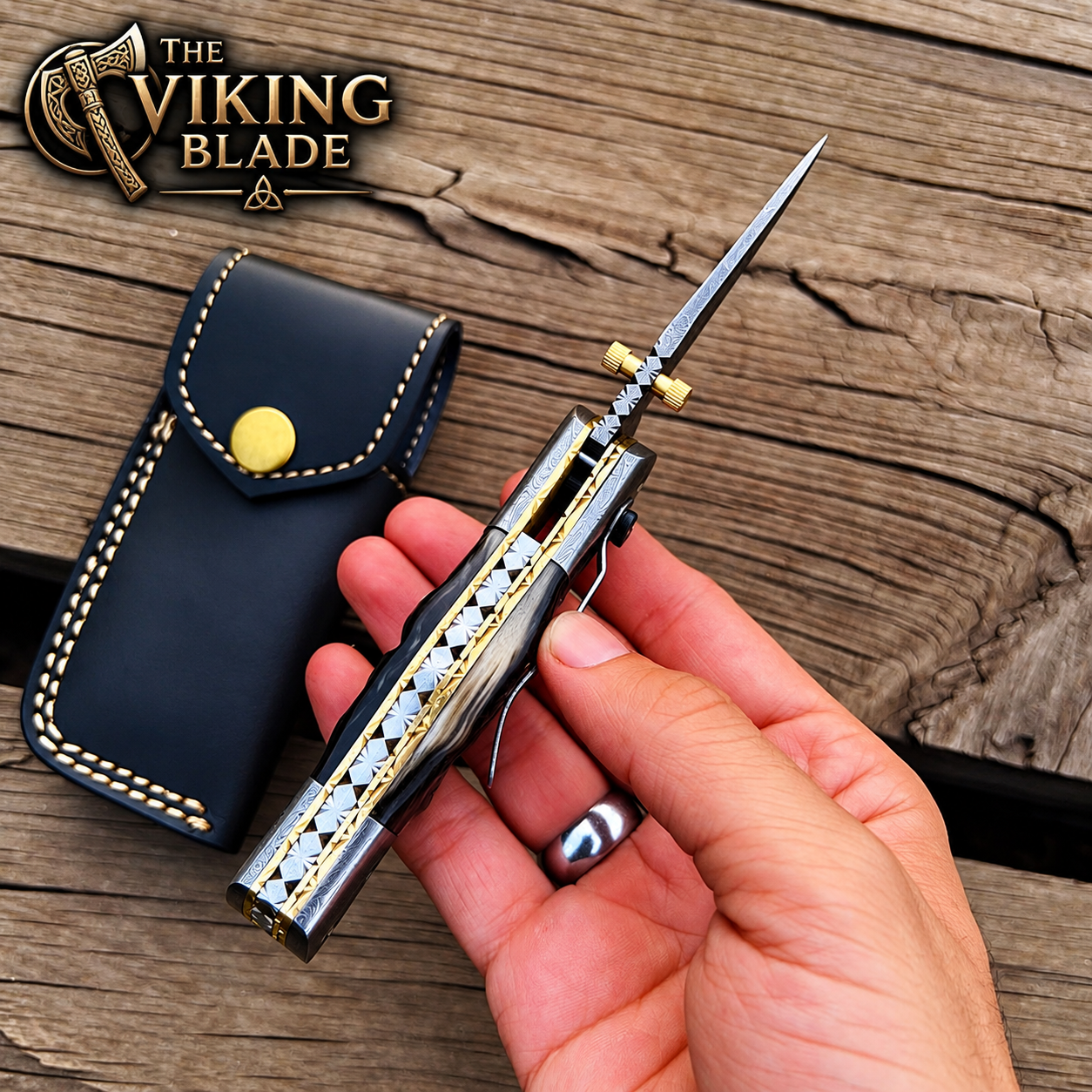 A hand holds a folding knife with a silver blade and geometric gold-and-black handle, next to a dark blue leather sheath with a gold snap. The background is a rustic wooden surface, and the logo 'The Viking Blade' is visible in the top left corner.