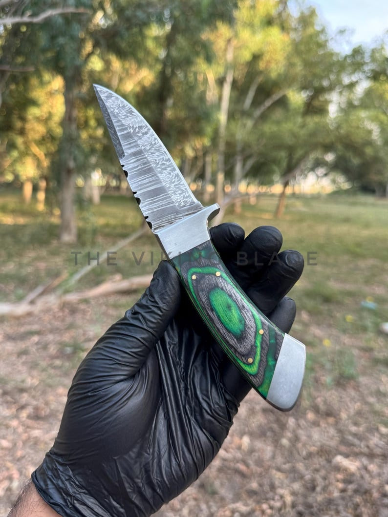 Knife with a green handle held by a gloved hand outdoors