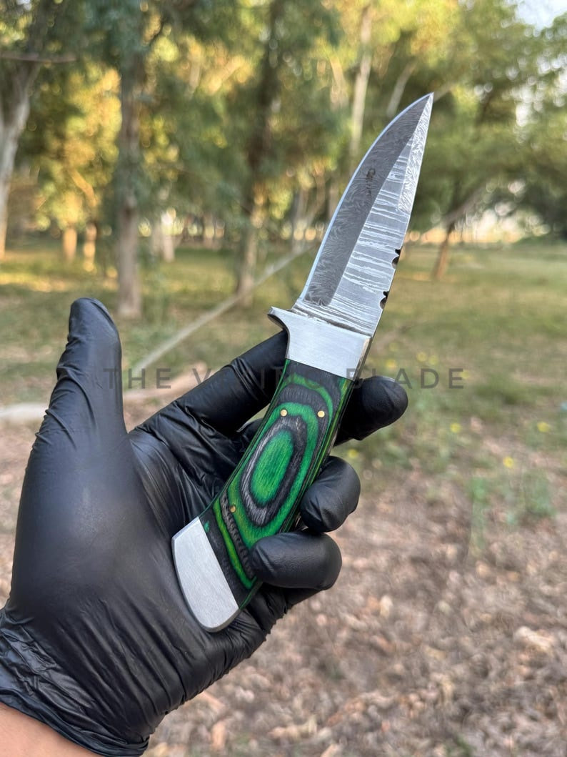 Knife with a green handle held by a gloved hand against a natural background