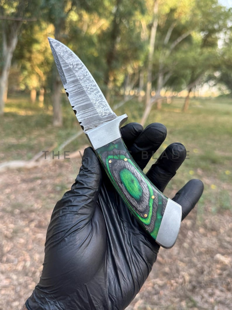 Knife with green handle held by a gloved hand in an outdoor setting