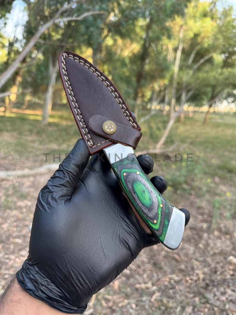 Knife with a leather sheath held by a gloved hand against a natural background