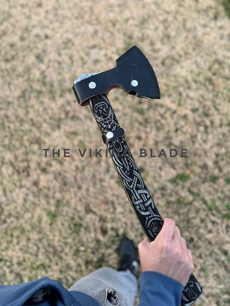 Person holding a decorative axe with 'The Viking Blade' branding against a grassy background