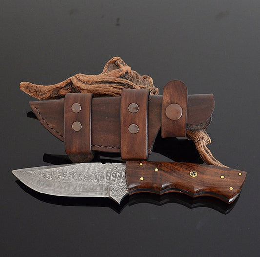 Hand-forged Damascus hunting knife with a brown wooden handle and brass accents, accompanied by a brown leather knife sheath.