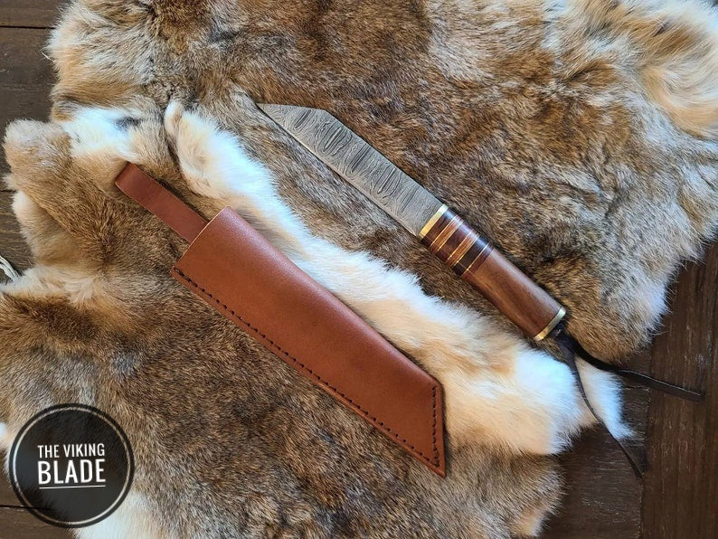 A Damascus steel knife with a walnut handle and decorative brass spacers, accompanied by a premium leather sheath, displayed on a faux fur surface.