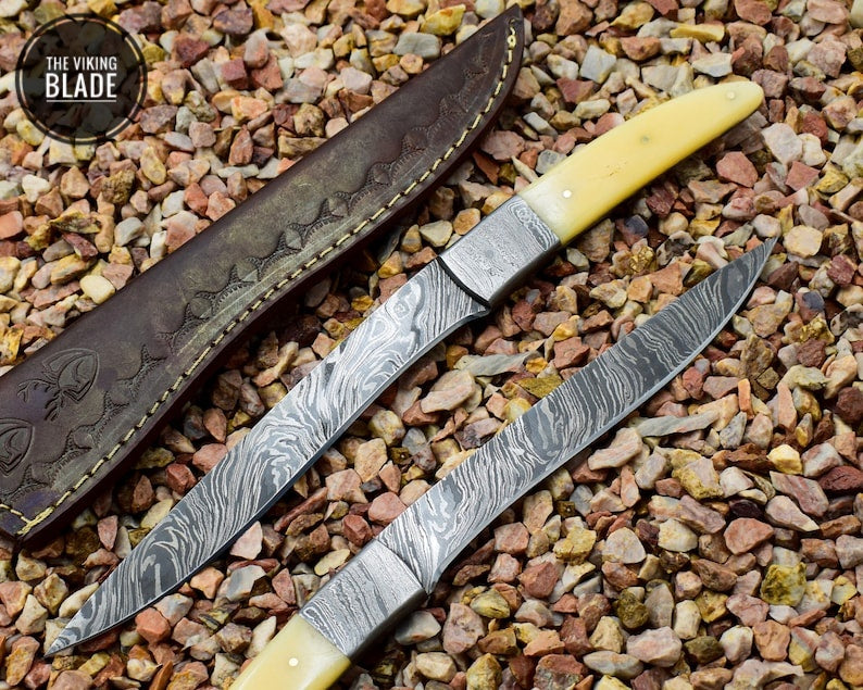 A handmade Damascus steel fillet knife with a camel bone handle and a patterned blade, displayed on a bed of pebbles.