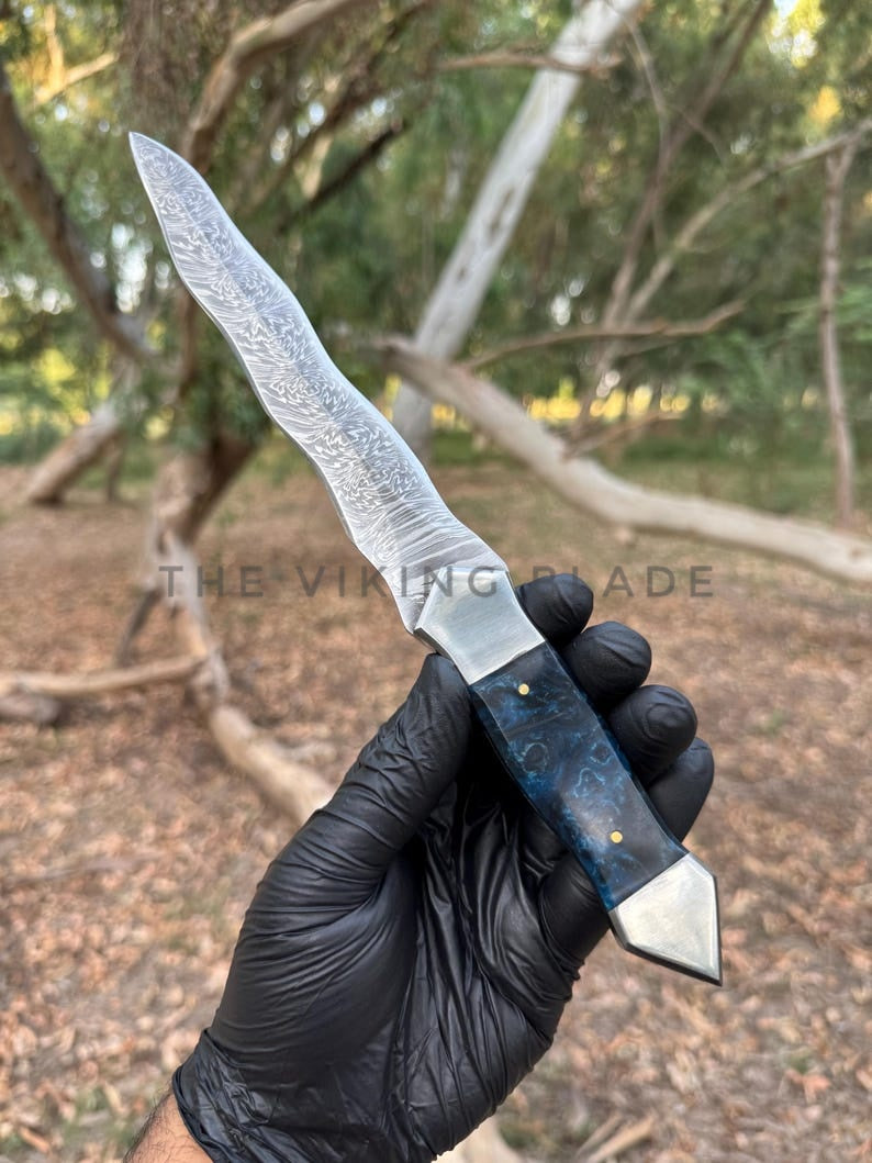 Knife held by a gloved hand with a forest background