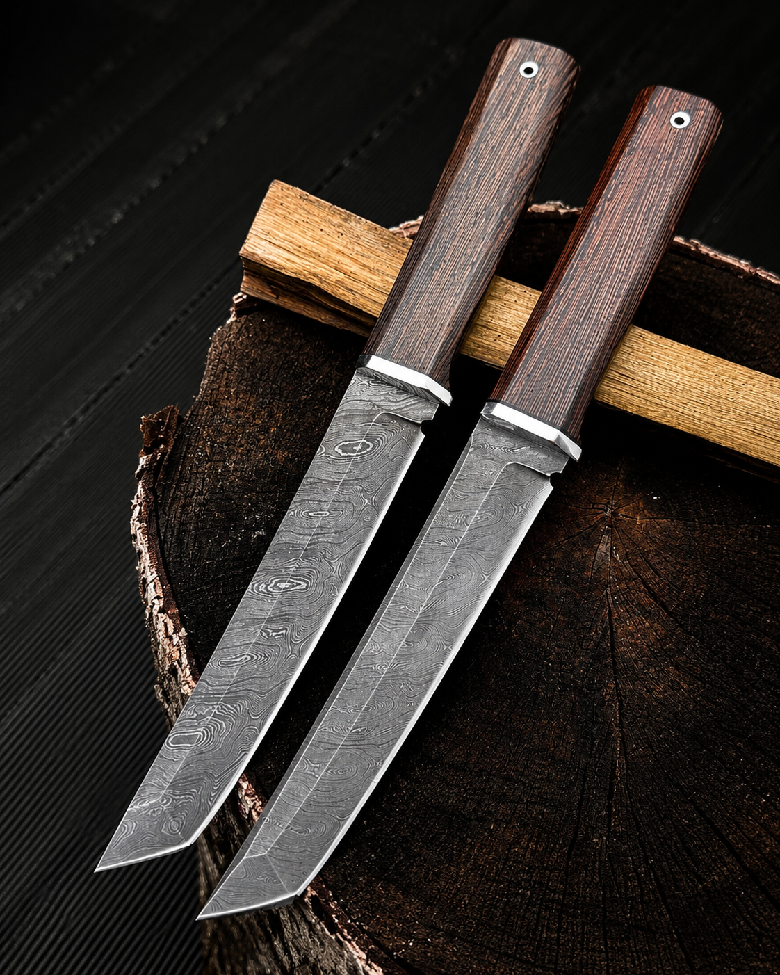 Two fixed-blade knives with patterned steel blades and dark brown wooden handles, displayed diagonally on a rustic wood slice against a dark wood background.