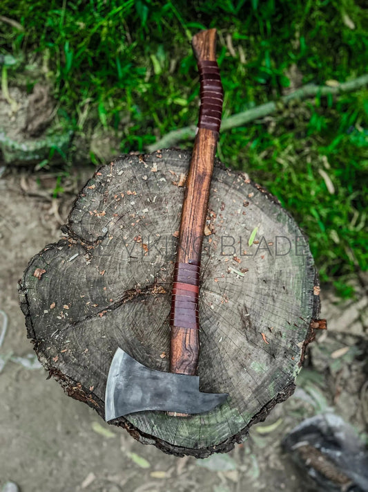 Axes with wooden handles on a tree stump with grass in the background