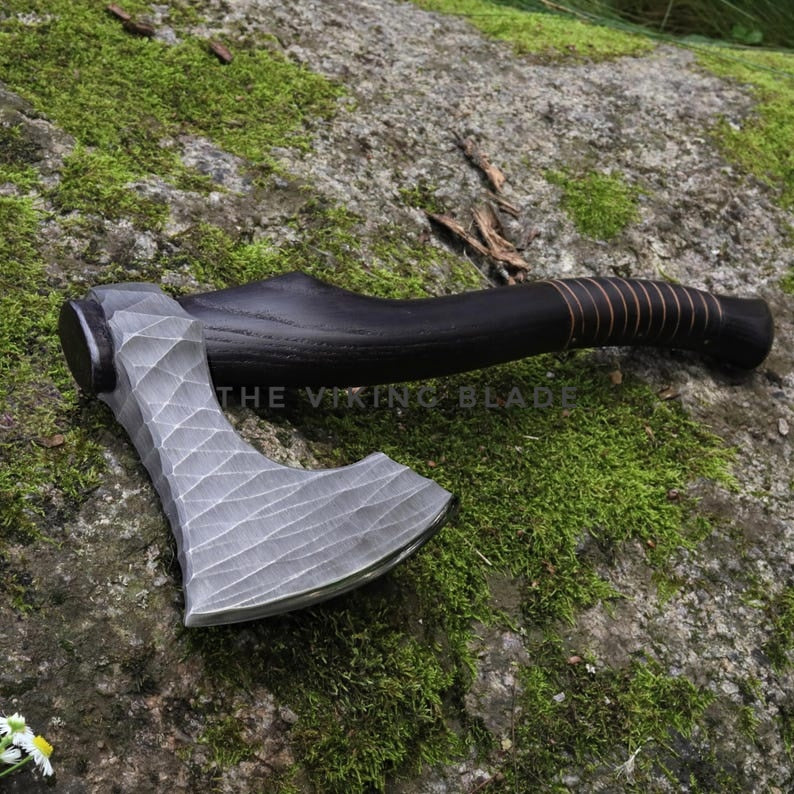 Axes with black handles and gray blades on a mossy stone surface, branded 'The Viking Blade'.