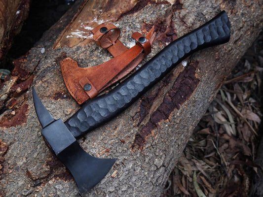 Black tomahawk with leather sheath on a wooden surface