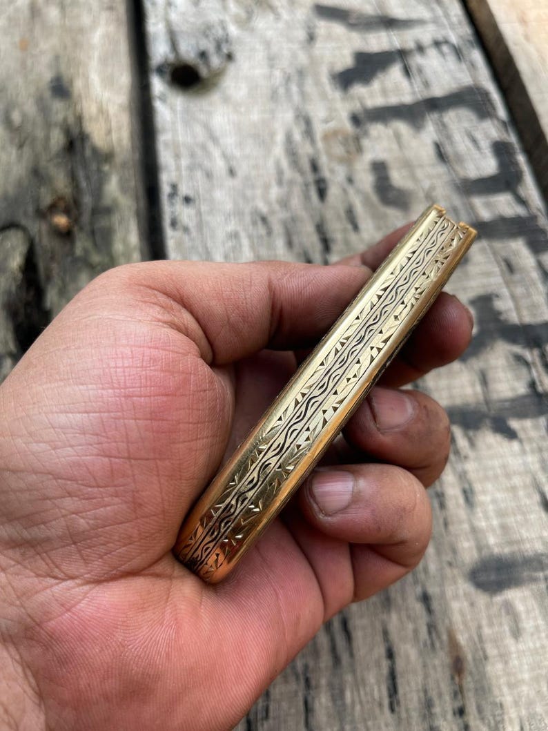 Hand holding a gold-colored object with intricate patterns against a wooden background