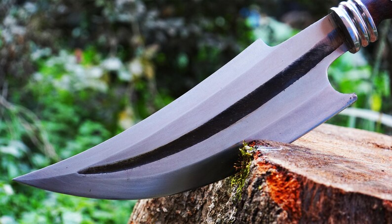 Knife with a silver blade and black handle on a wooden stump with a blurred natural background