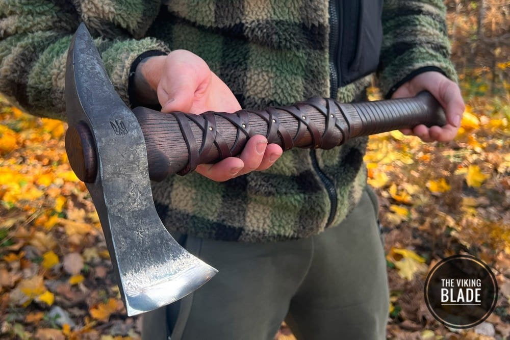 Hand-forged Gurons spike tomahawk with a steel head and an ashwood handle, held in a hand with a leather cover on the handle.