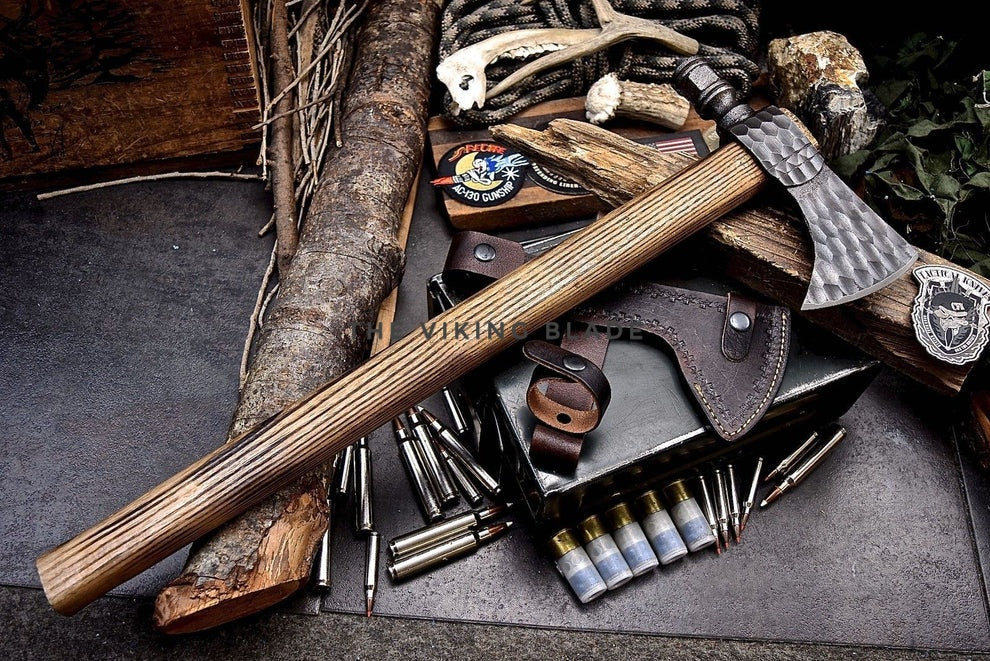 Collection of hunting tools including axes, bullets, and a leather pouch on a stone surface.