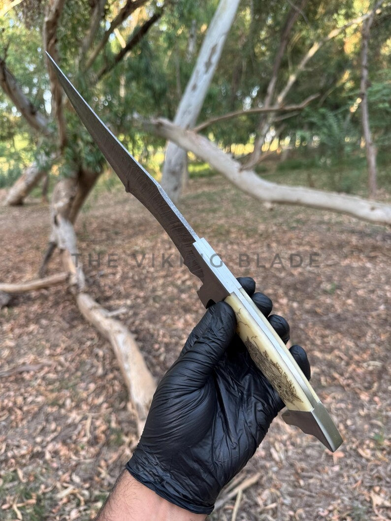 Hand holding a knife with 'The Viking Blade' branding outdoors.