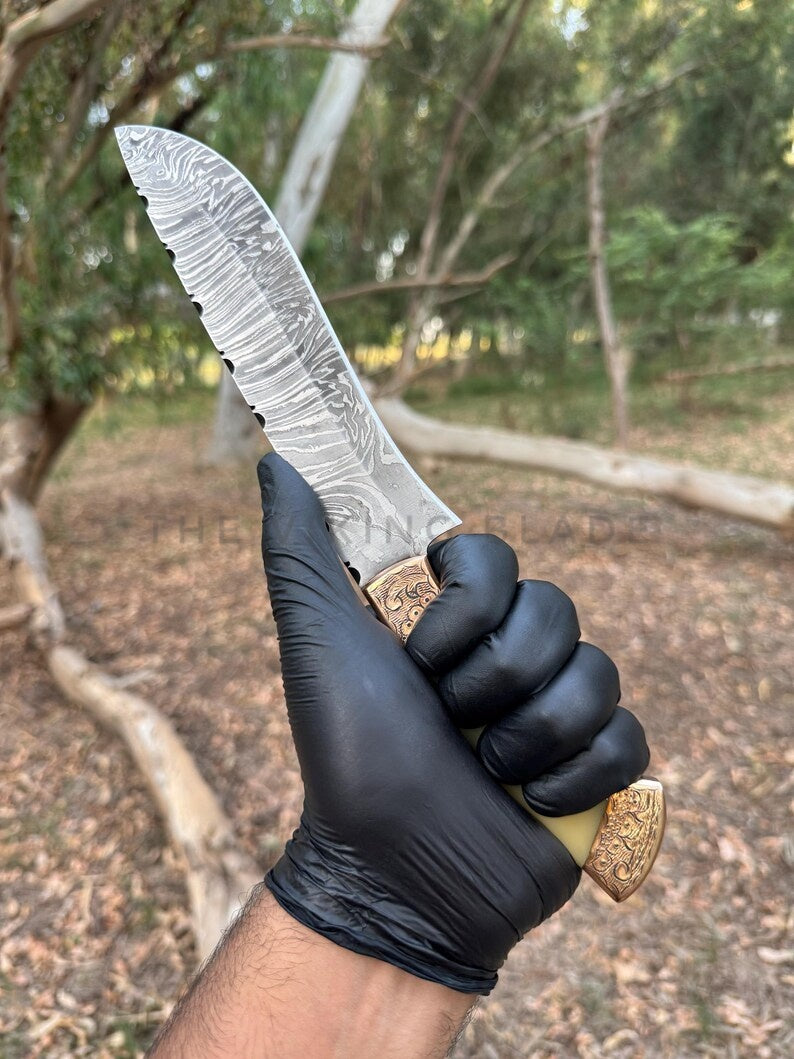 Hand holding a knife with a detailed blade in a black glove, outdoors.