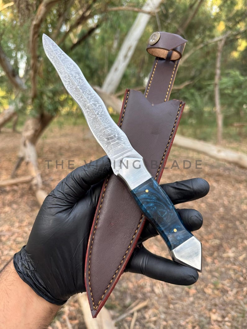 Knife with leather sheath held by a gloved hand against a natural background